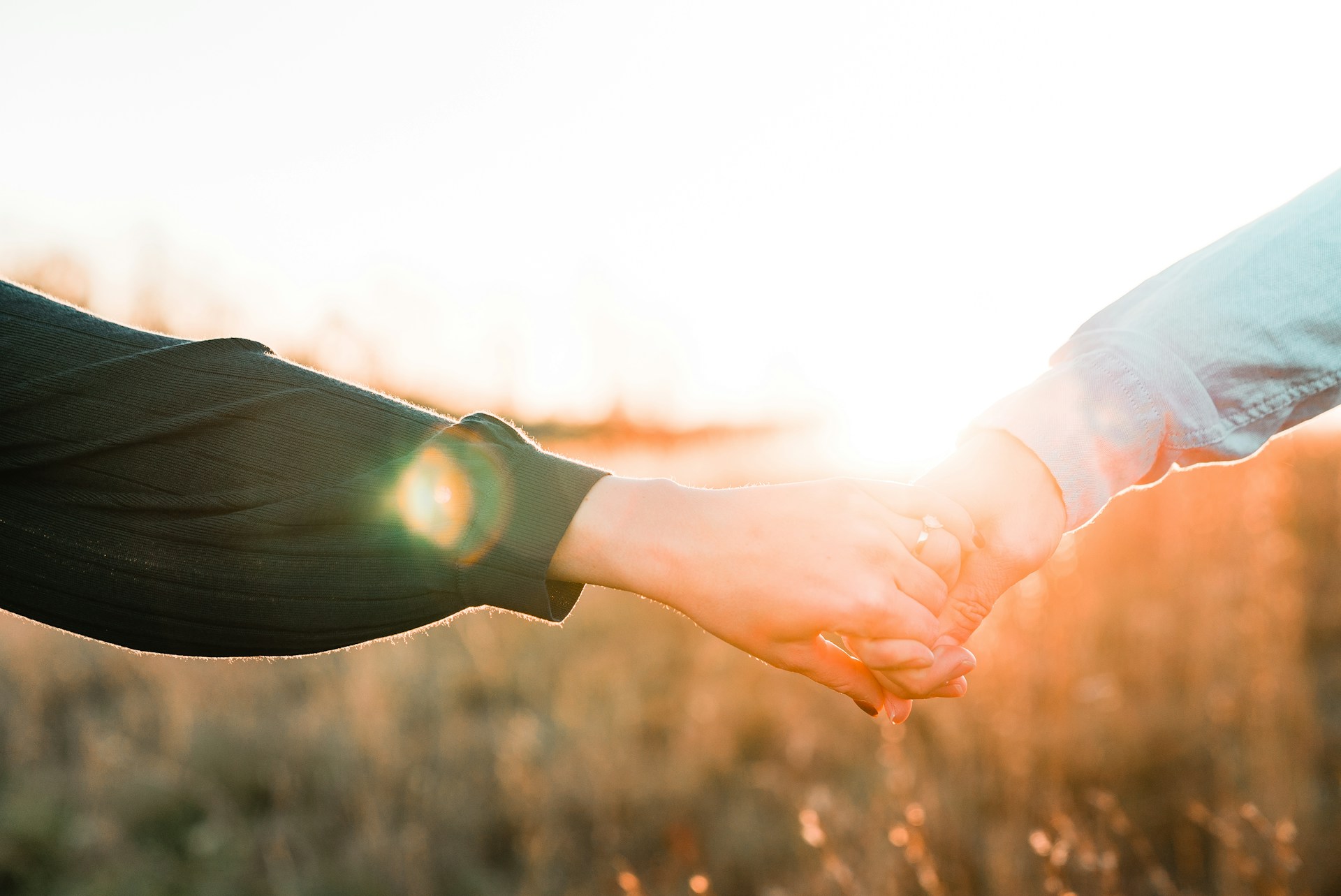 two people holding hands in a field with the sun shining behind